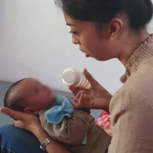 Priscilla Valayodapillai holding and feeding a baby on her lap at Tamar House.