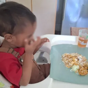A toddler in a high chair enjoying lunch during the Tamar House support visit.
