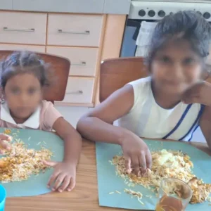 Two smiling young girls eating lunch together at Tamar House during a charity support visit.