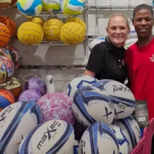 Nadia Coward and store assistant with a cart full of rugby, soccer, and netballs being prepared for donation.